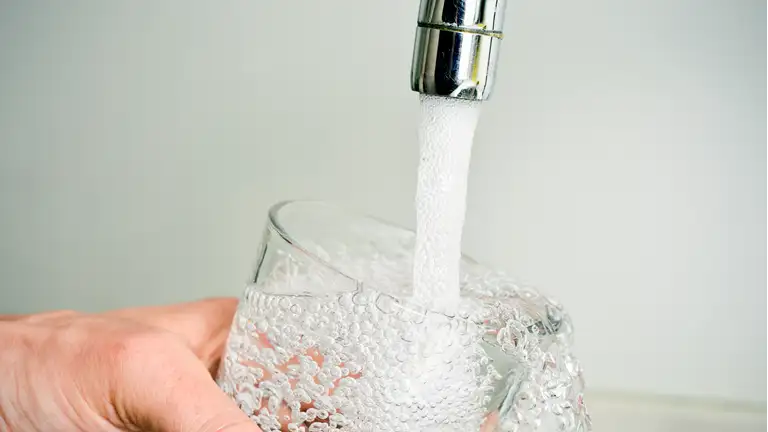 en person fylder et glas med vand fra vandhanen